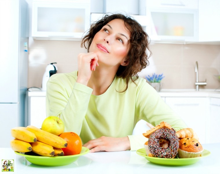 Young woman thinking with green plates of fruit and donuts and pastries in a white kitchen.