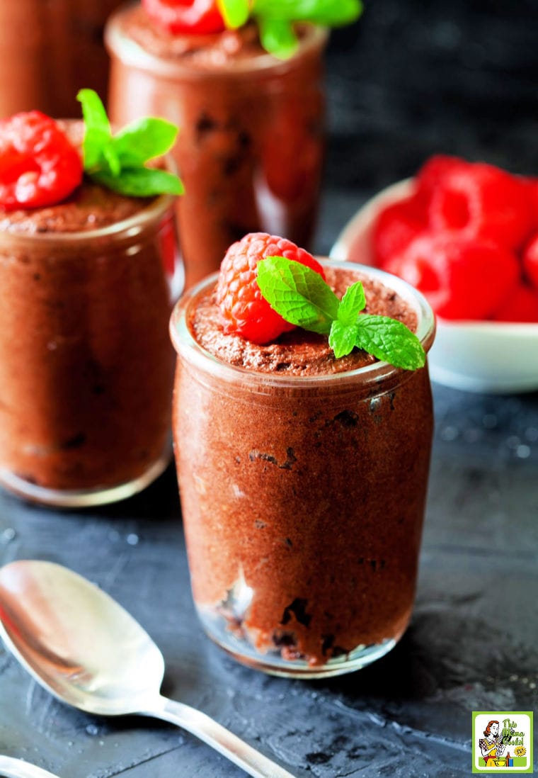 Chocolate mousse in a small glass with a garnish of raspberries and mint with bowl of raspberries in the background.