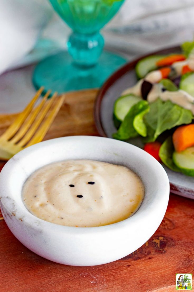 Vegan Salad Dressing Recipes - a small bowl of Spicy Sesame Ginger Vegan Salad Dressing with salad and a gold fork on a wooden cutting board
