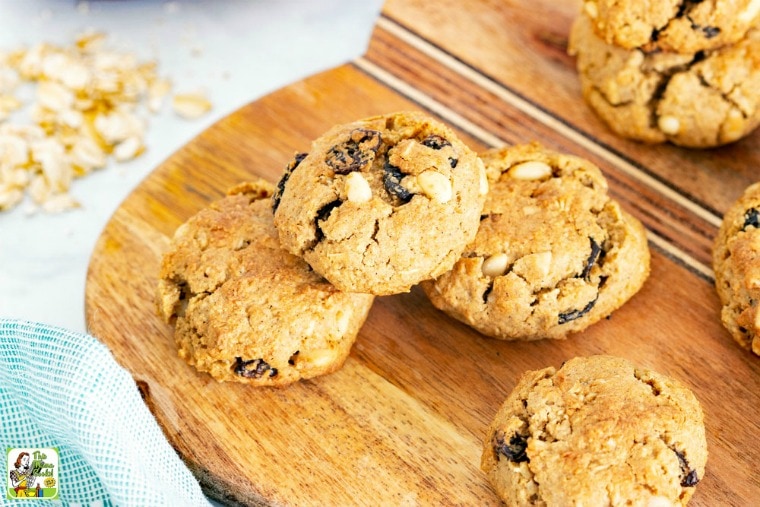 Cookies with pine nuts and raisins on a cutting board with a wooden spoon and baking ingredients.