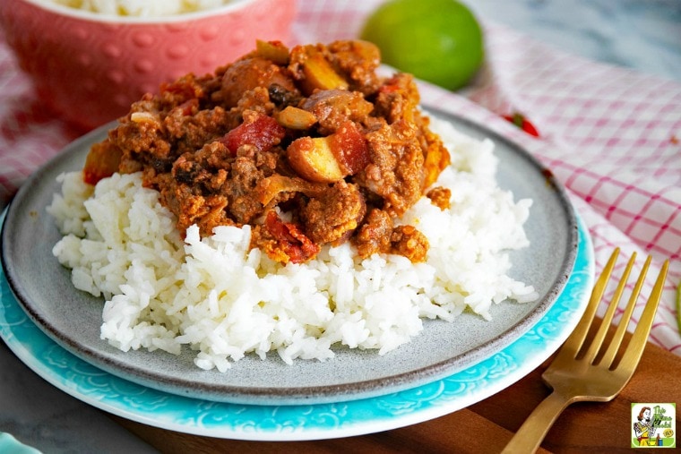 A plate of Mexican Picadillo on white rice with fork, napkin, and lime.