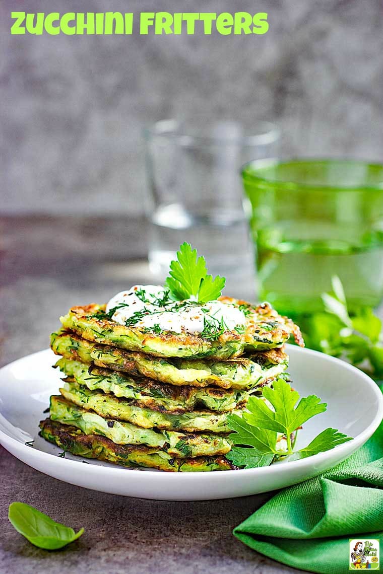 A plate of Zucchini Fritters topped with sour cream and fresh herbs.