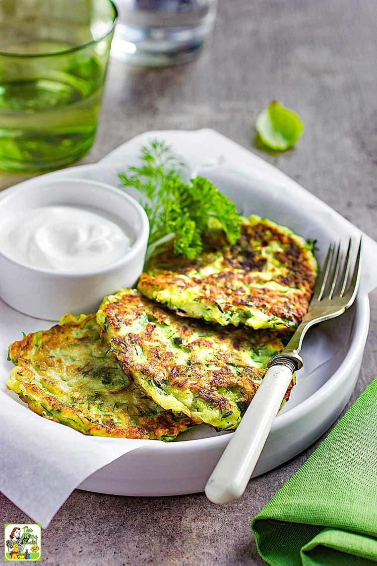Plate of Zucchini Fritters with bowl of sour cream and a fork.