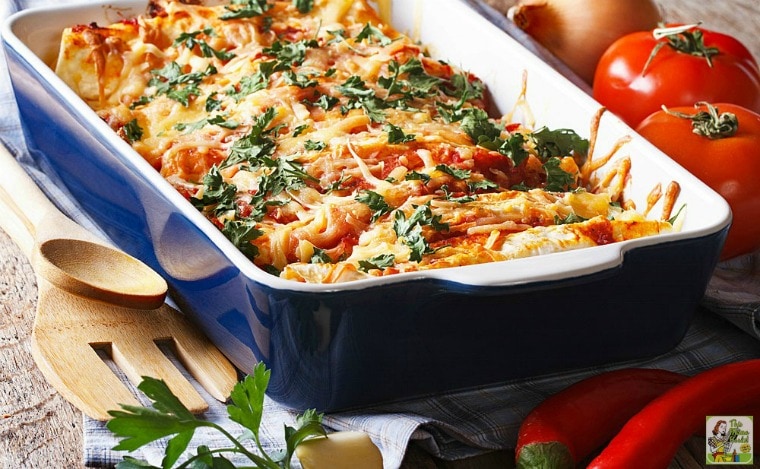 Turkey Enchilada Casserole in a blue baking dish with wooden serving spoons, tomatoes, red peppers, and onions.