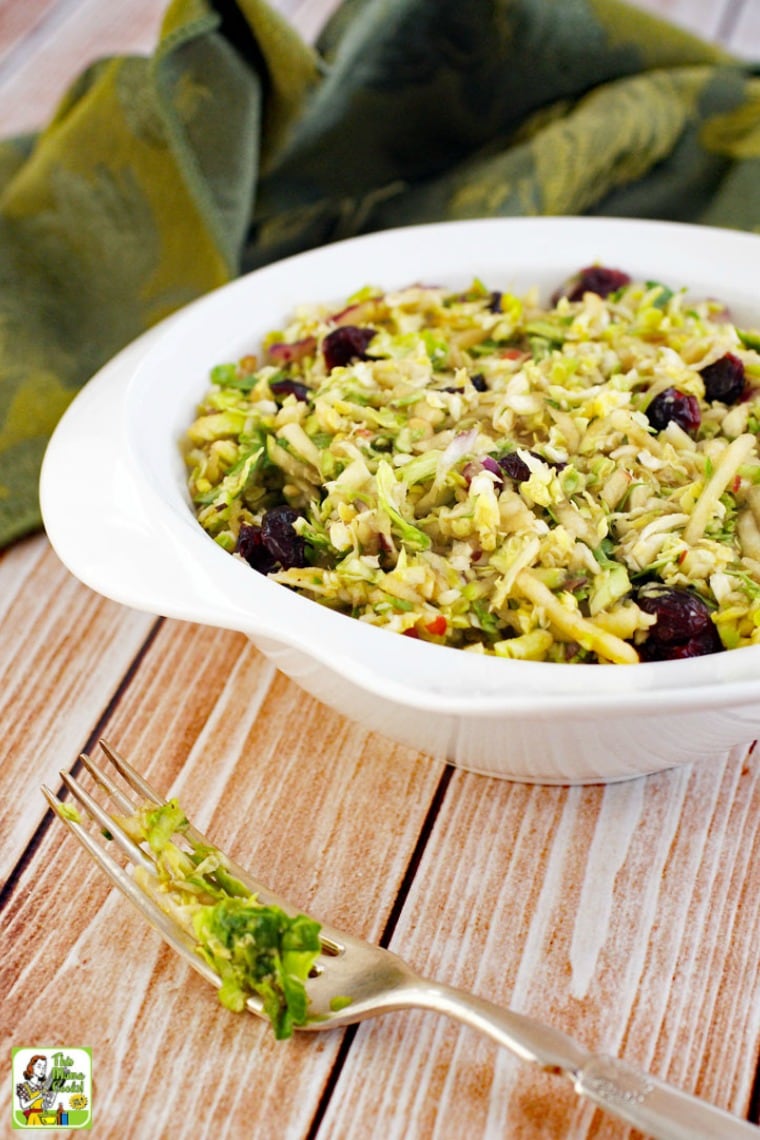 A white bowl of shredded brussel sprouts salad with cranberries, green napkin, and a fork.