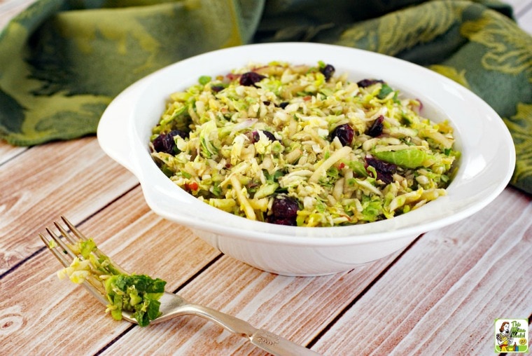 A white bowl of shredded brussel sprouts salad with cranberries with green napkins.