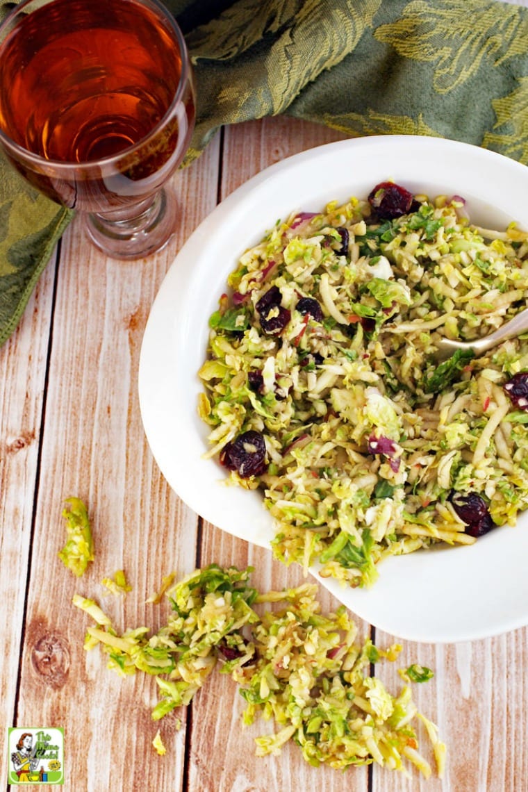 A white bowl of shredded brussel sprouts salad with cranberries with a glass of iced tea.