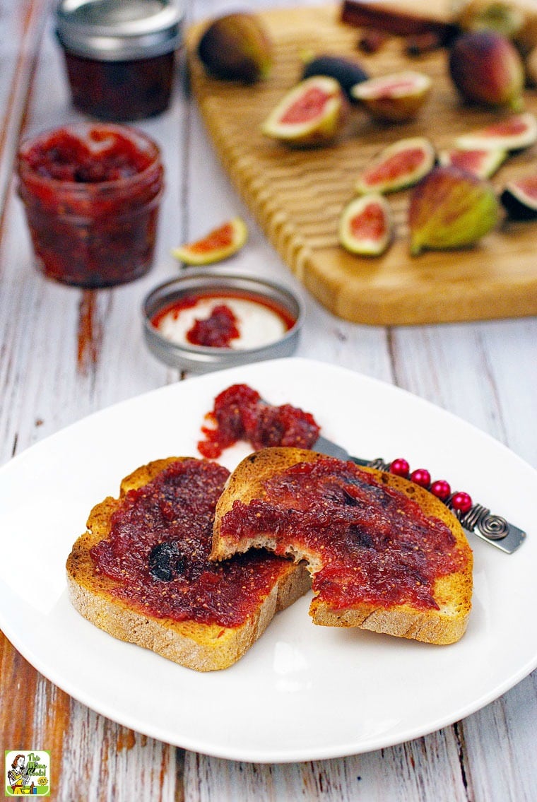 Toast with fig jam on a plate with a jar of fig jam and figs in the background.