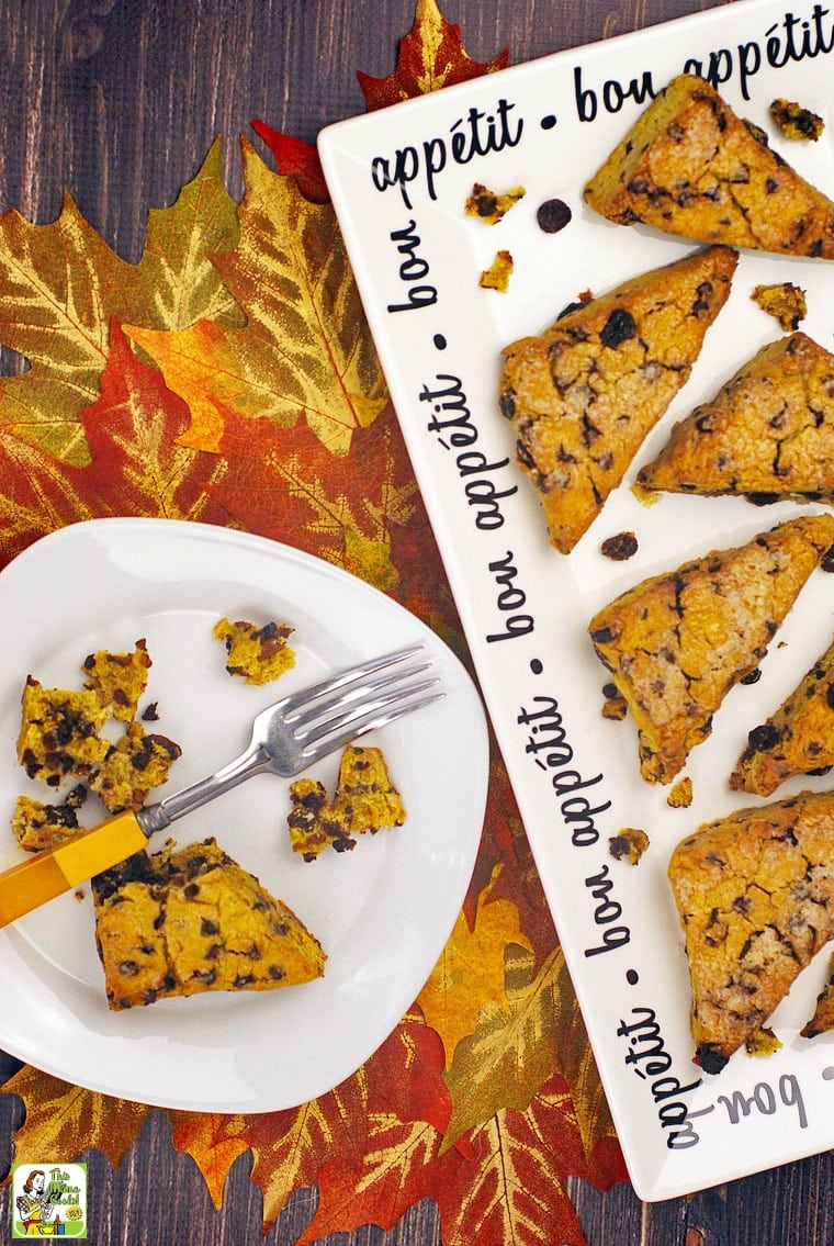 A white plate and platter of gluten free pumpkin scones with fork on a table of fall leaves.