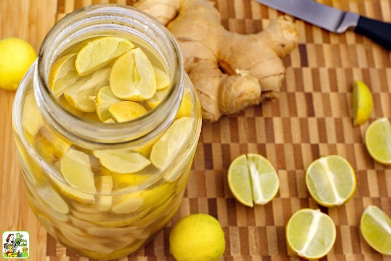 A large mason jar of Lime & Ginger Infused Vodka with limes, ginger, and knife on a wooden cutting board.