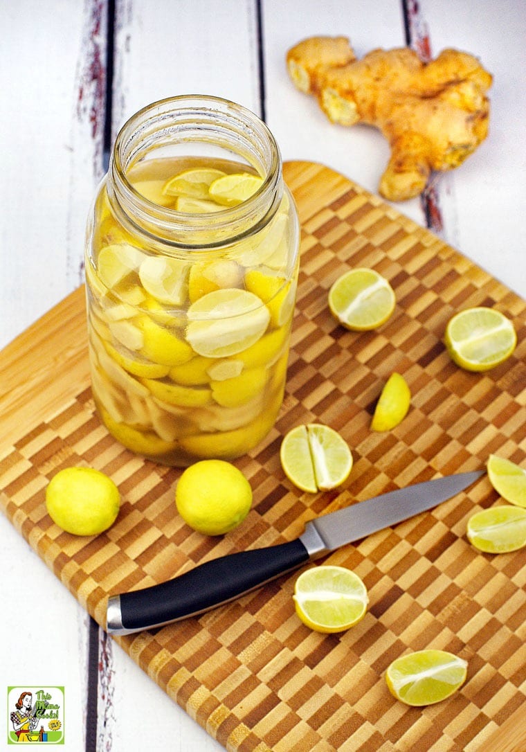 A mason jar of infused vodka on a wooden cutting board with limes, ginger and a pairing knife.