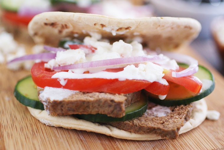 A homemade gyros sandwich with feta, sliced onion, slice cucumber, and tzatziki sauce on a wooden platter.