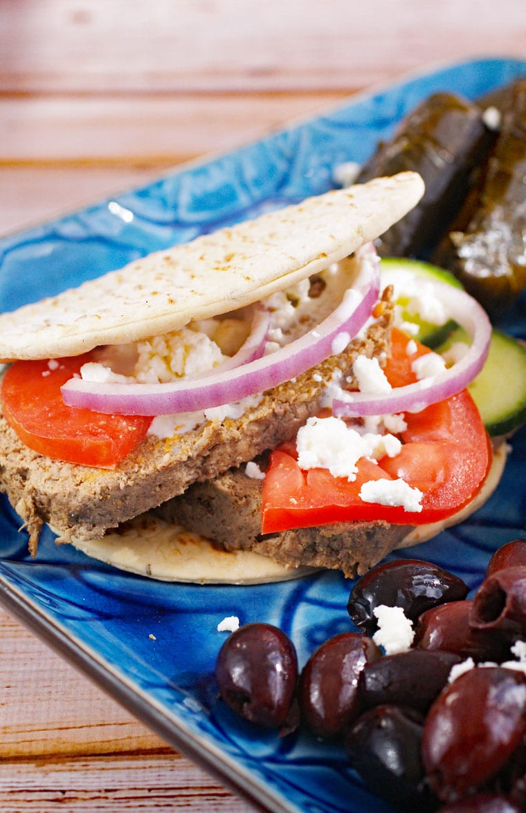A gyro sandwich on pita with olives and dolmades on a blue platter.