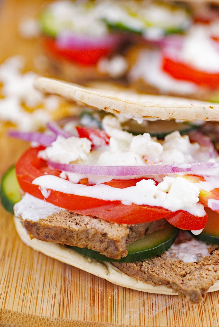 Closeup of a authentic Greek gyros sandwich with tomatoes, feta, onions, and cucumbers on a wooden platter.