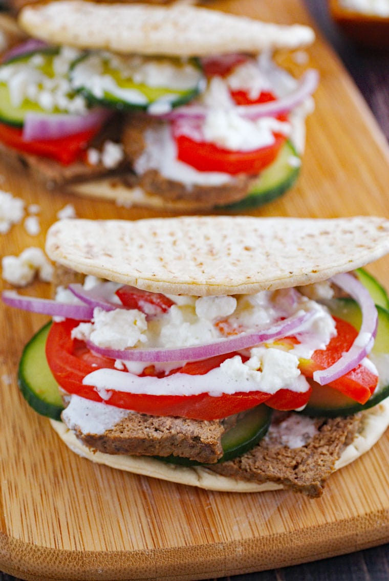 Two authentic homemade Greek gyros sandwich with tomatoes, feta, onions, and cucumbers on a wooden platter.