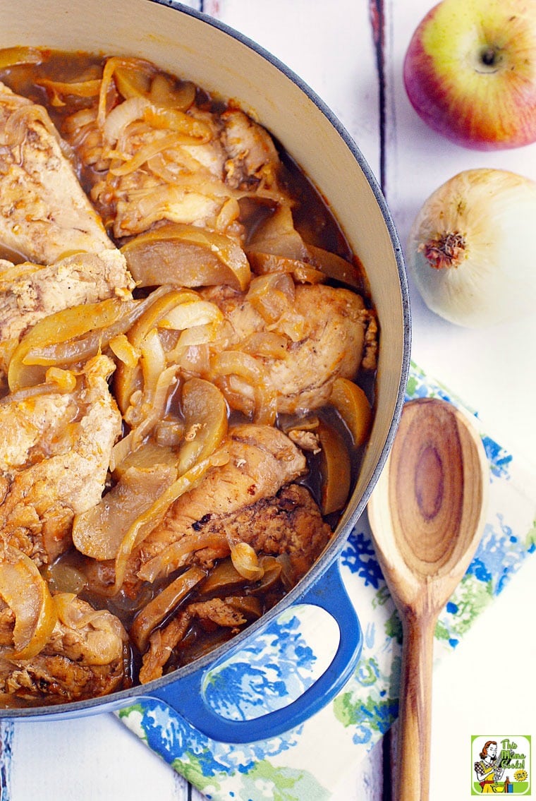 A blue Dutch oven filled with chicken and onion stew with a wooden serving spoon and floral napkin. 