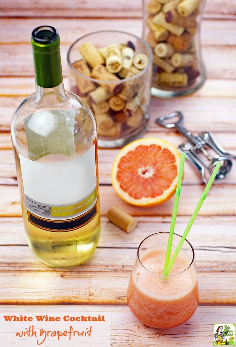 A glass of white wine cocktail with straws, with grapefruit with a wine bottle, grapefruit, winecorks, and wine bottle opener.