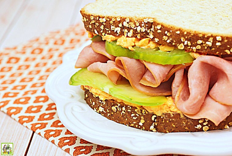 A Ham & Pimento Cheese Sandwich on a white plate with an orange patterned napkin.