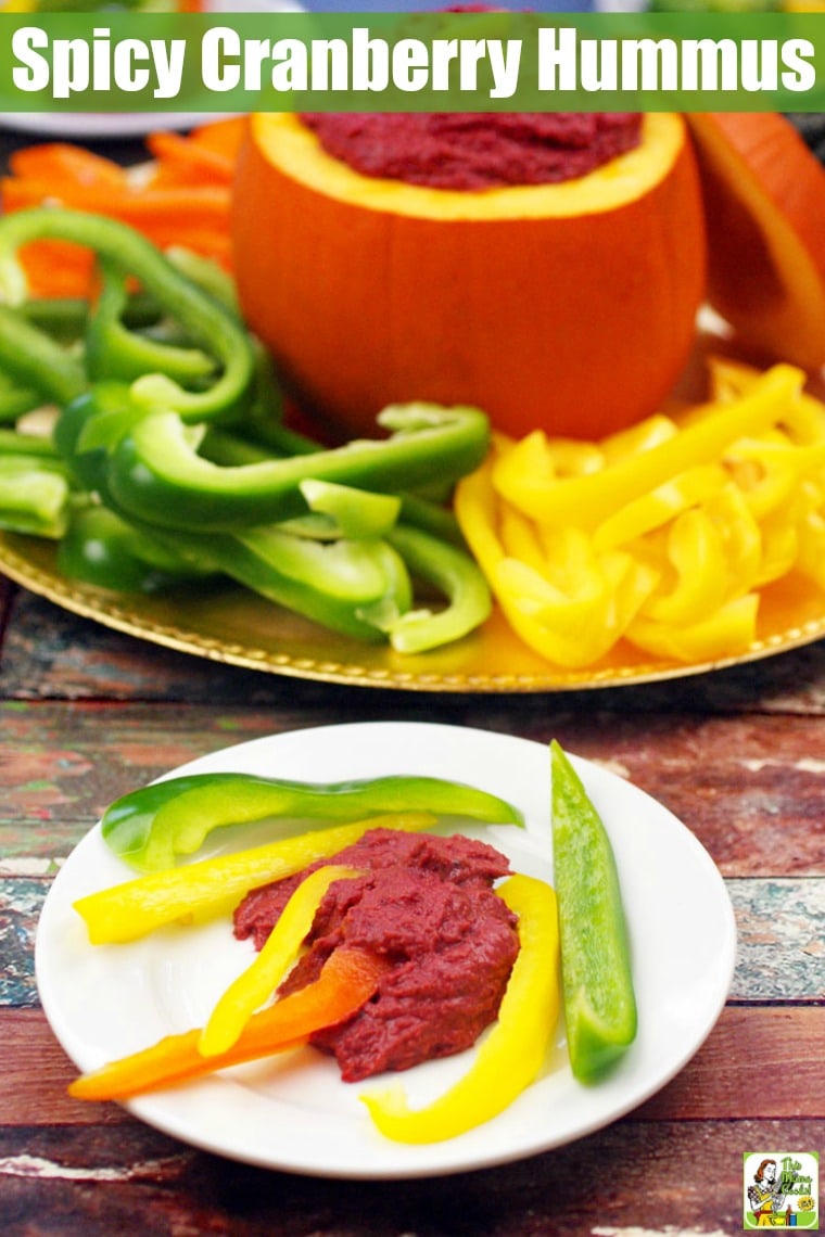 A white appetizer plate of sliced peppers and hummus and a large serving platter of peppers and Cranberry Hummus in a small pumpkin.