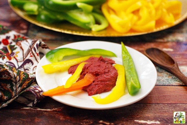 A white appetizer plate of sliced peppers and hummus.