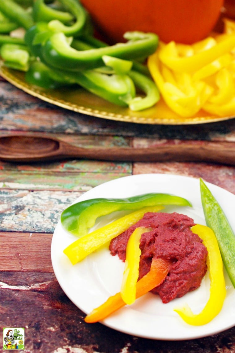 A white appetizer plate of sliced peppers and hummus and a large serving platter of peppers and hummus.