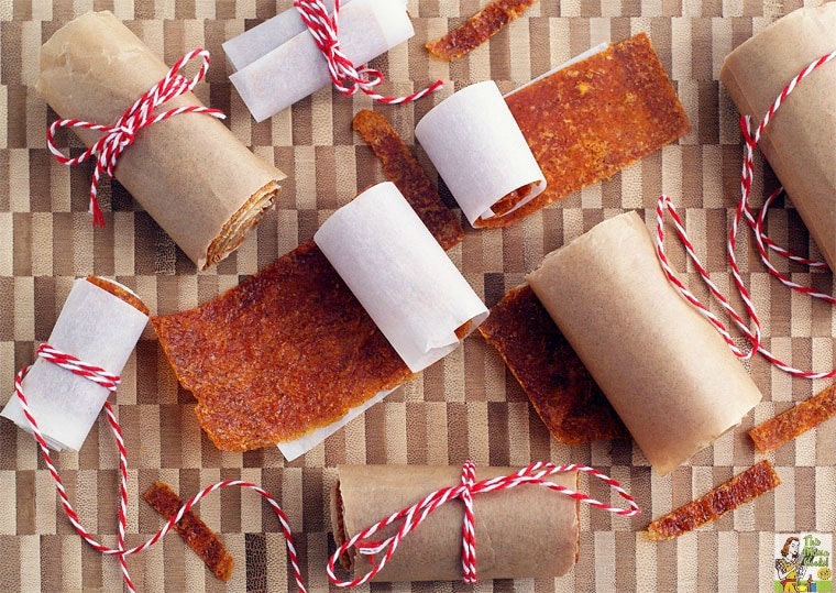 Rolls of Orange Fruit Leather tied in kitchen twine on a wooden cutting board.