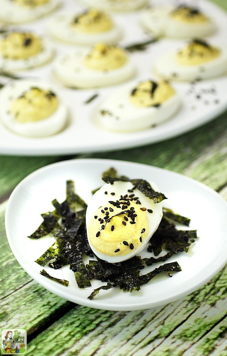 Closeup of a small plate of a deviled egg with strips of dried seaweed and black sesame seeds.