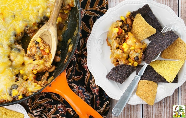 A skillet and plate of Easy Nachos with serving spoon, tortilla chips, and fork.