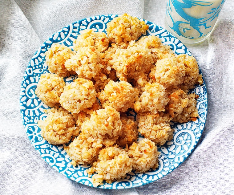 An overhead shot of a white and blue plate of golden coconut macaroons with a blue glass of milk on a white cloth.