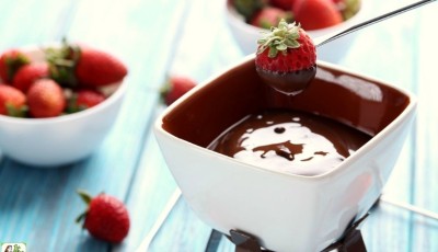Dipping strawberries into a small pot of chocolate fondue on a candle warmer with bowls of strawberries in the background.