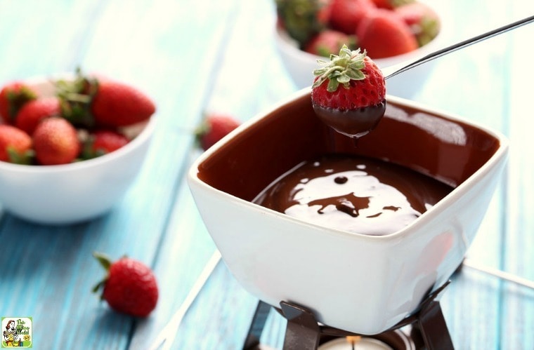 Dipping strawberries into a small pot of chocolate fondue on a candle warmer with bowls of strawberries in the background.