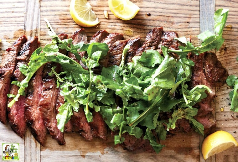 Grilled Flank Steak on a cutting board with arugula and lemon slices.
