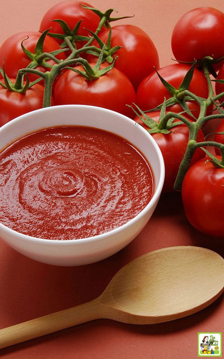 A bowl of freshly made tomato sauce, a wooden spoon, and tomatoes on the vine.