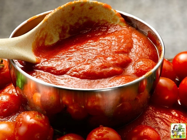 A bowl of Alton Brown's tomato sauce with wooden spoon and tomatoes.