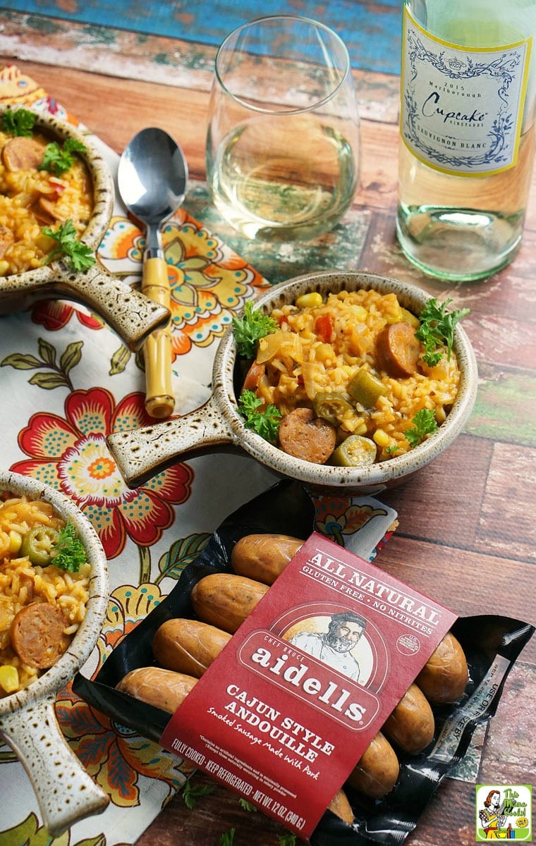 Bowls of jambalaya, a package of Aidells Aindouille sausage, a wine glass, a bottle of wine, and spoons on a colorful napkin.