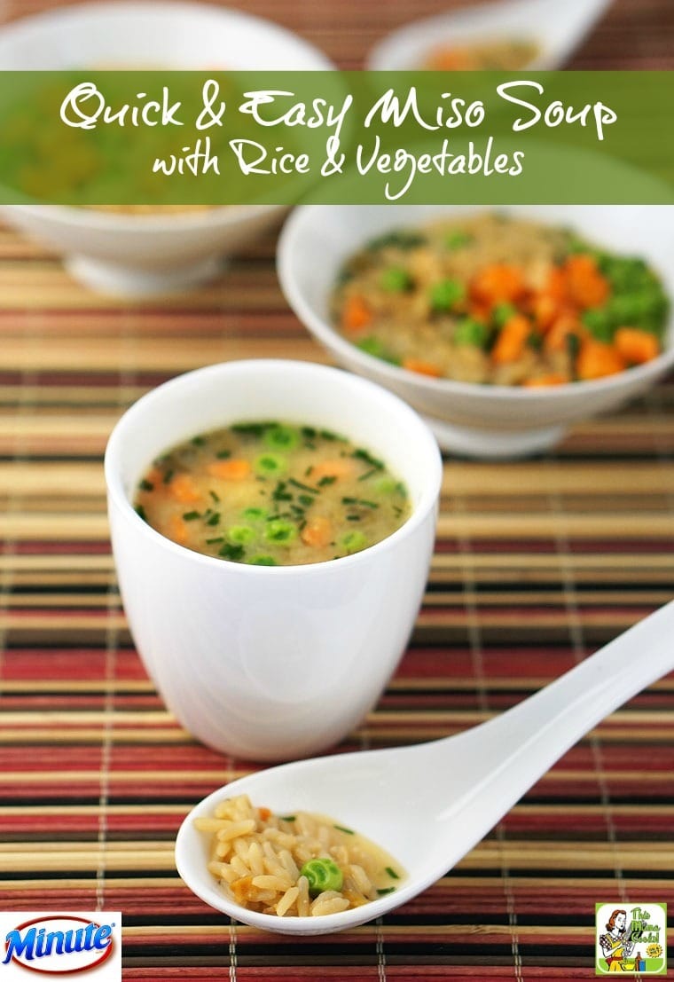 Bowls and a cup of miso soup with rice, peas and carrots and a soup spoon on a colorful woven mat.