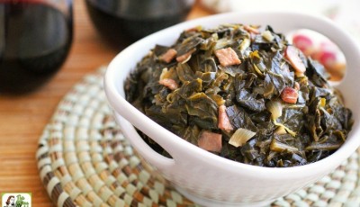 A white bowl of easy sweet collard greens on a woven mat with red wine glasses in the background.