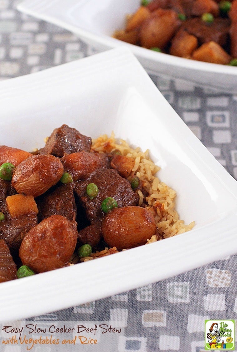 A closeup of a bowl of beef stew with peas, carrots, potatoes and rice. 