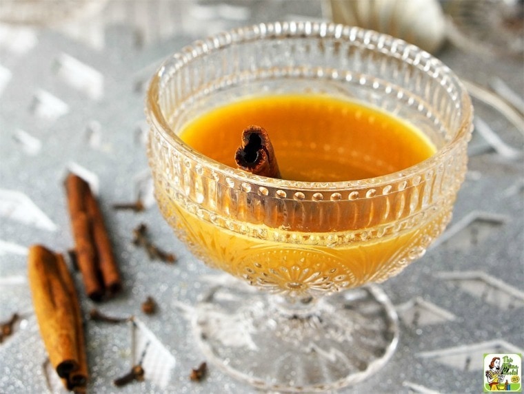 A glass of spice autumn tea with cinnamon sticks on a silver placemat. 