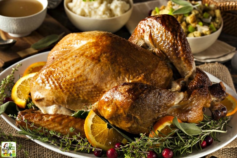 A cooked Thanksgiving turkey on a whites platter with orange, cranberries, and herb garnish surrounded by holiday side dishes.