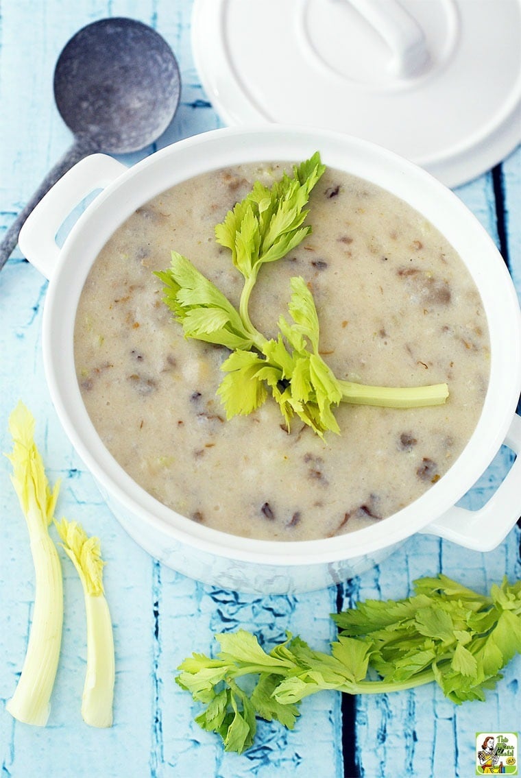 A bowl of Easy Dairy Free Oyster Chowder with lid, celery stalks, and ladle on a blue tabletop.