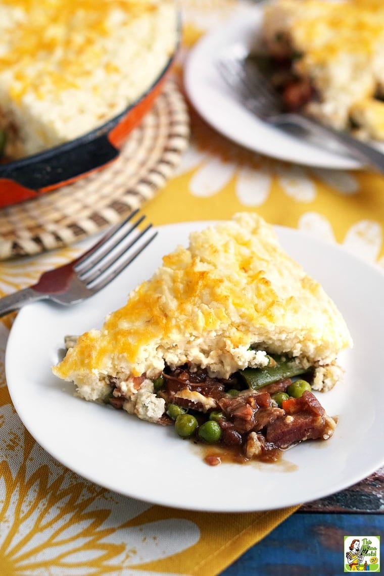 Slice of pot pie with peas, carrots, green beans and ham on a white plate with a fork