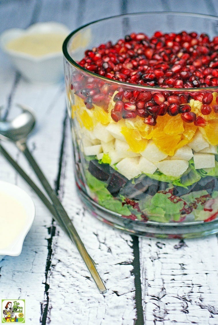 A layered Mexican Christmas Salad in a glass bowl, a dish of dressing, and salad tongs.