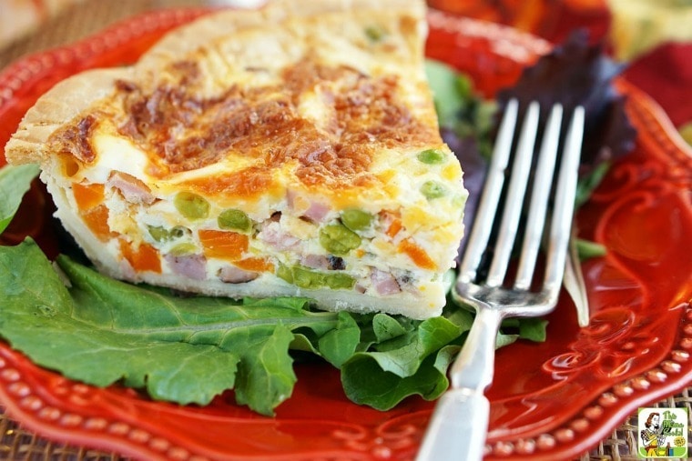 A red plate with a slice of quiche, salad, and a fork.