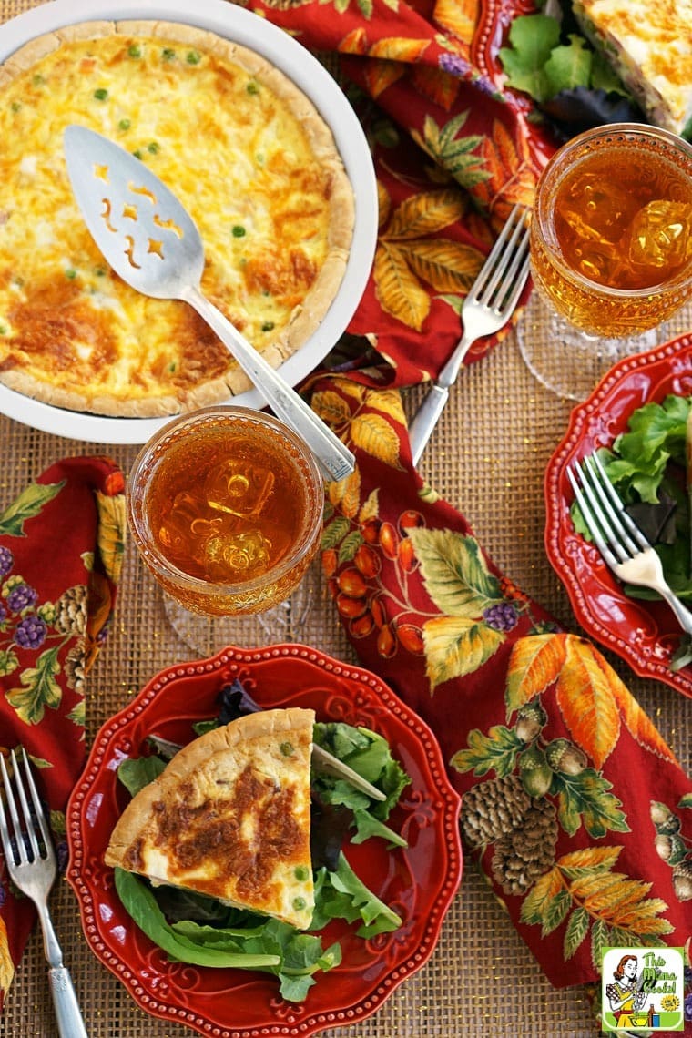 Plates and a pie plate of quiche with a glasses of iced tea, salad, colorful napkins, forks and serving knife.