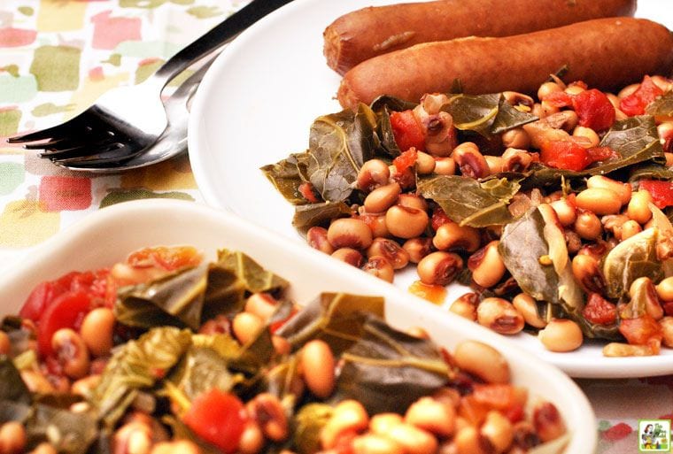 Closeup of a white dish and plate of hoppin john black-eye peas and collard greens with tomatoes and a fork.