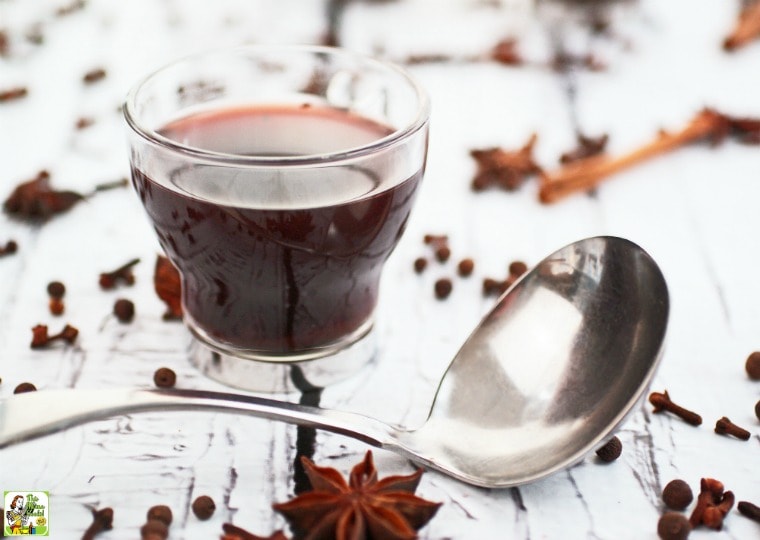 A glass of mulled wine with ladle and spices.