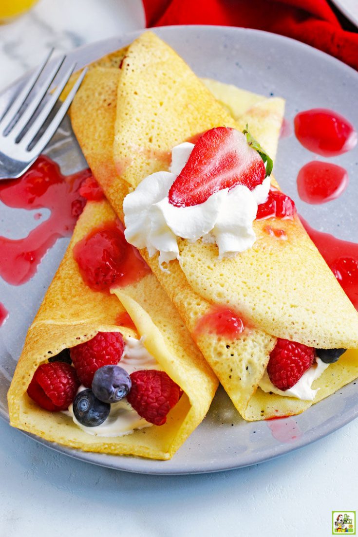 Closeup of two crepes on a plate stuffed with berries and whipped cream.