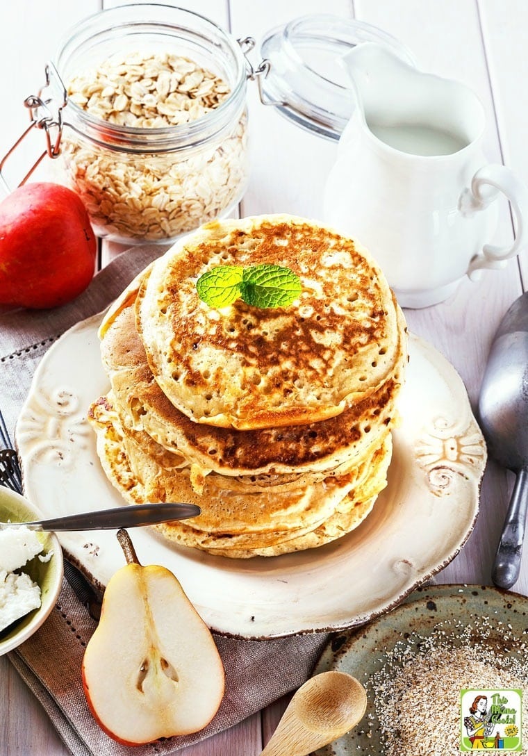 A stack of High Protein Oatmeal Pancakes on a plate with pears, cream cheese, and a jar of oats.