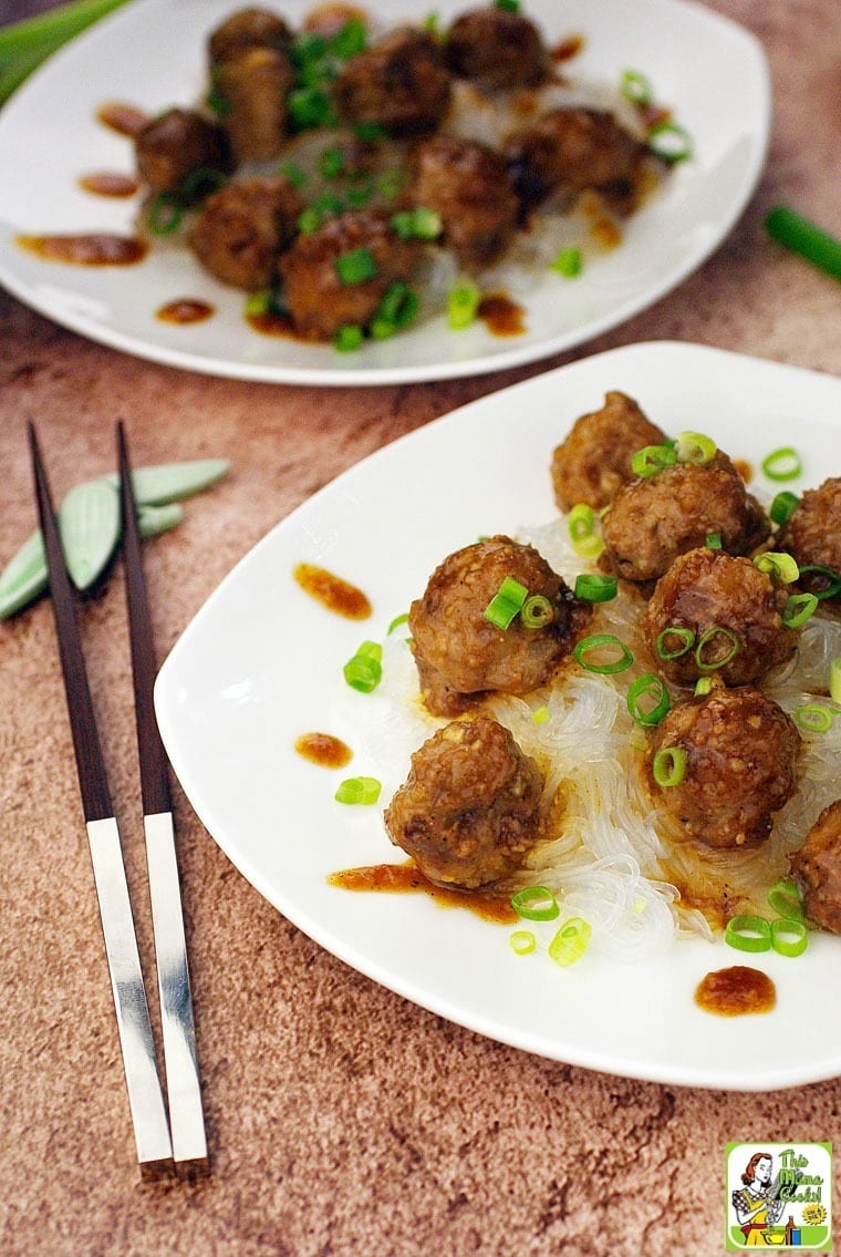 Closeup of Asian Meatballs with Hoisin Sauce on a white plate with chopped green onions and chopsticks.